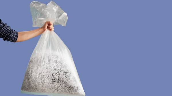 A person holding a trash bag of shredded paper.